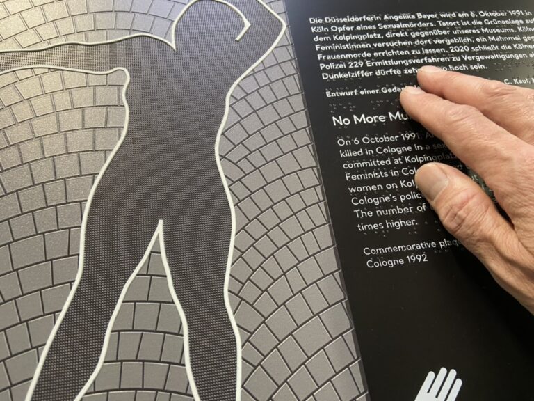 Das Bild zeigt eine Grafik als taktiles Exponat für Alle, mit Erklärungen in Braille und Schwarzschrift. Eine Hand berührt die Punktschrift.